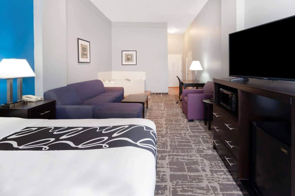 Une chambre d’hôtel avec un lit, un canapé, un bureau, une télévision et, au fond, une salle de bain.