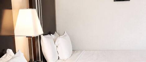 A hotel room with two beds, a nightstand with a lamp, a phone, and a wall-mounted picture.