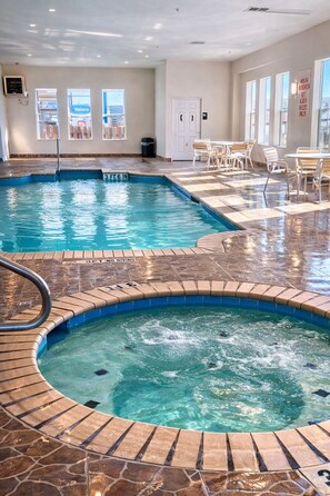 An indoor swimming pool with a hot tub, tiled flooring, and a seating area with tables and chairs.