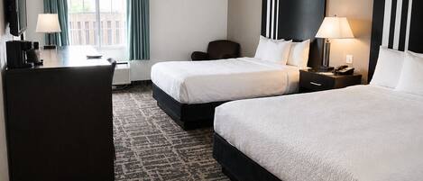 A hotel room with two beds, a desk with a chair, a TV, and a window with curtains.