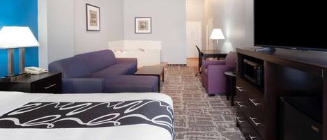 Quarto de hotel com cama, sofá, escrivaninha com computador, televisão e banheiro com banheira.