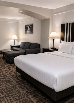 Una habitación de hotel con una cama grande, un sofá, dos mesitas de noche con lámparas, una alfombra estampada y un cuadro en la pared.
