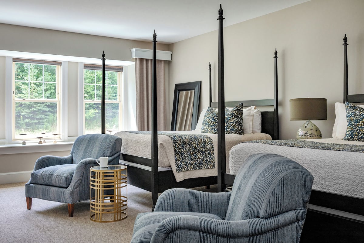 A bedroom with a four-poster bed, two armchairs, a bedside table, and a window with curtains.