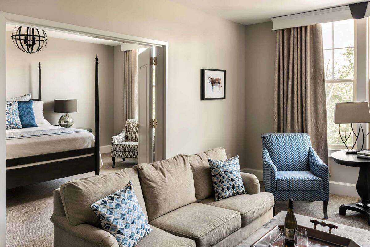 A hotel room with a bed, a sofa, a chair, a table with a lamp, and a window with curtains.