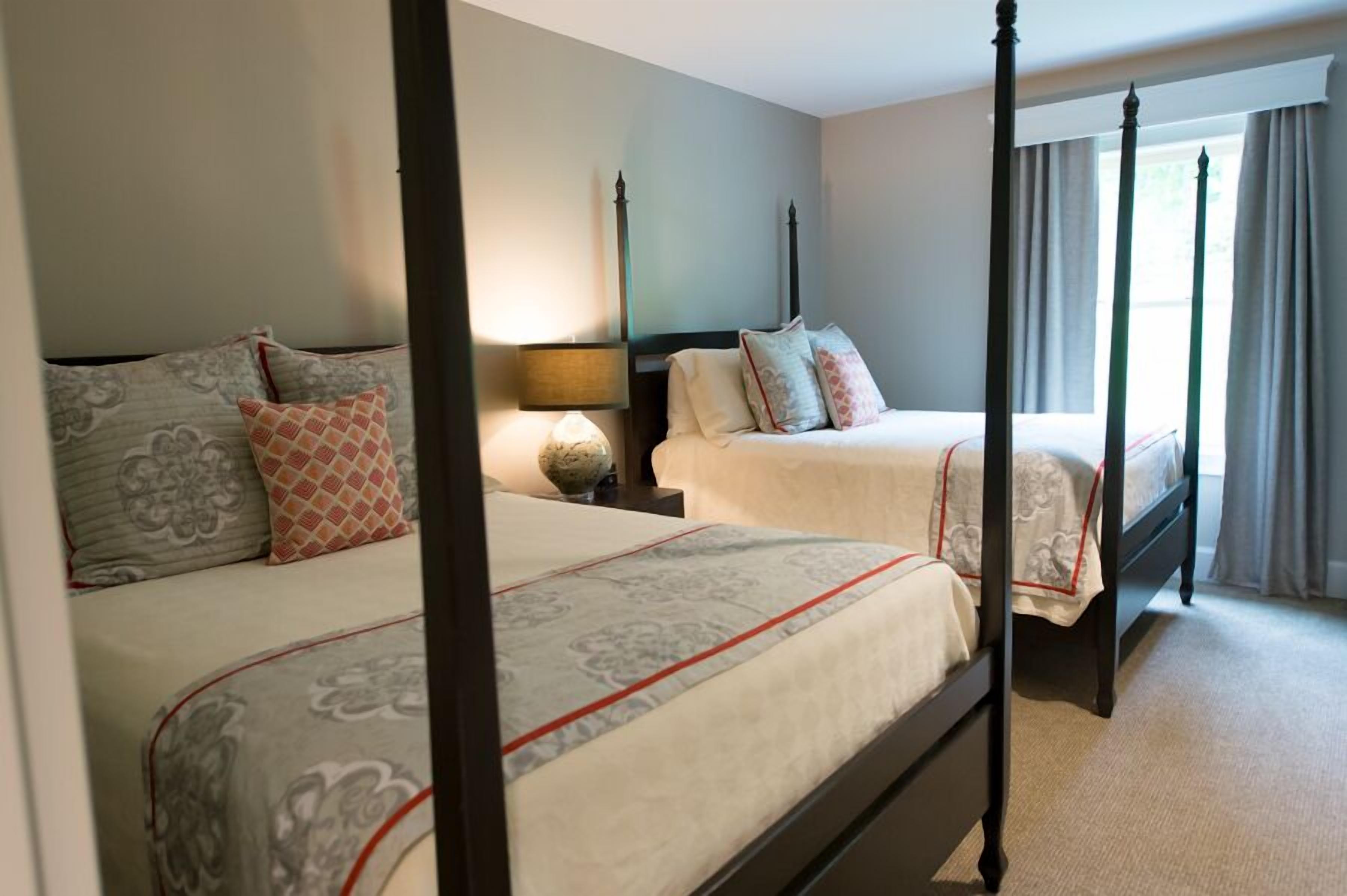 A four-poster bed with a nightstand, a lamp, and a window with curtains.