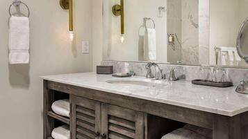 Un baño con tocador de doble lavabo, estantes de madera con toallas, un espejo grande y apliques de pared.