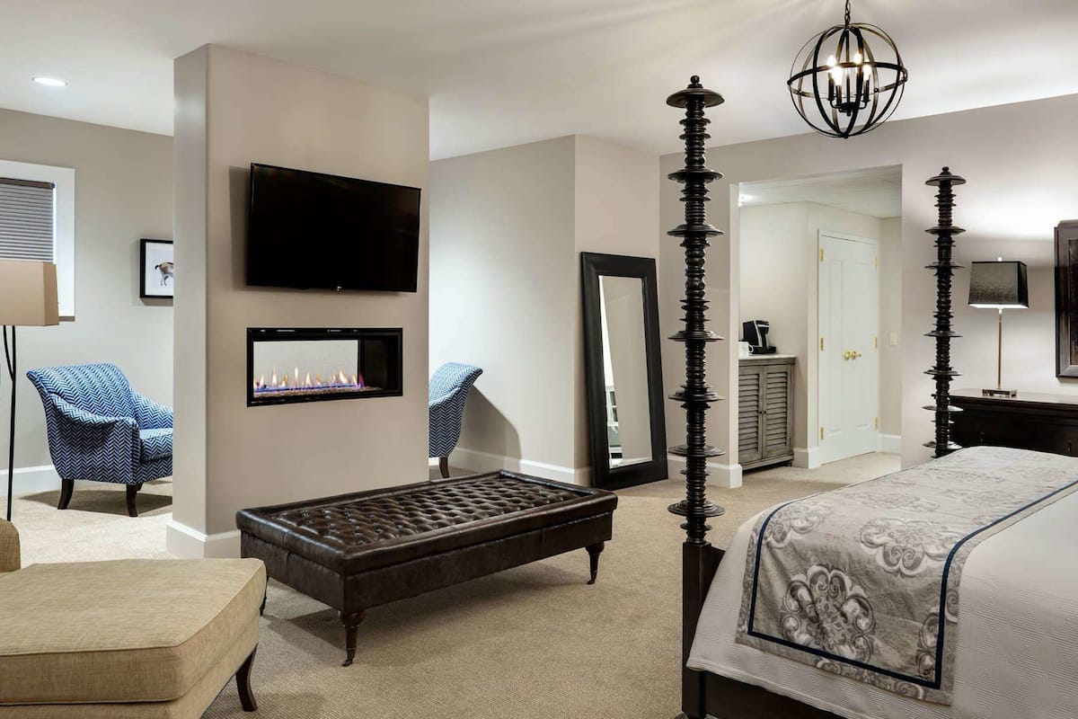 A bedroom with a large bed, a TV mounted on the wall, a fireplace, and a chandelier.