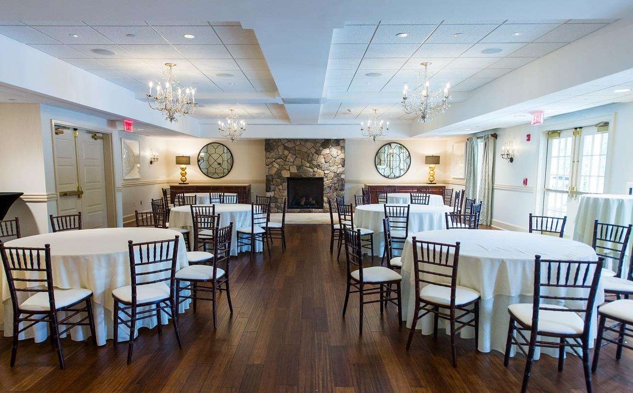 A spacious dining area with round tables and chairs, a stone fireplace, and chandeliers.