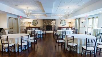 A spacious dining area with round tables and chairs, a stone fireplace, and chandeliers.