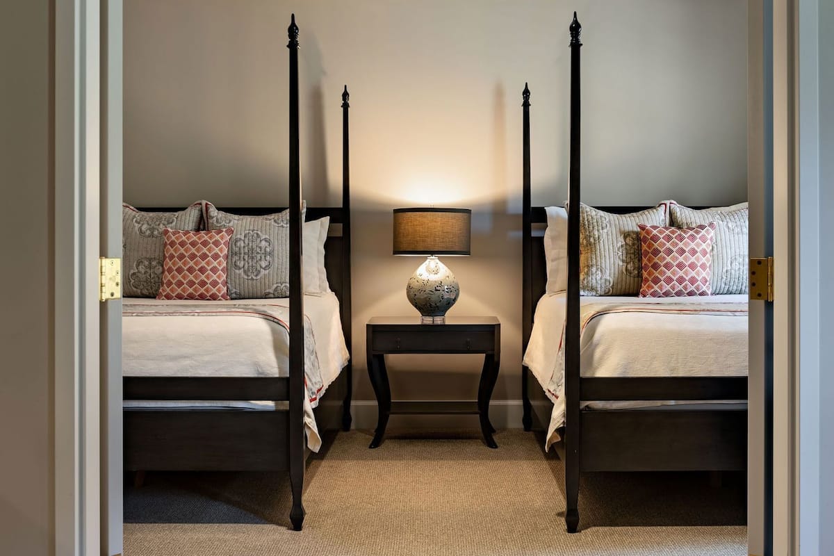 A bedroom with two beds, a nightstand with a lamp, and a door frame.