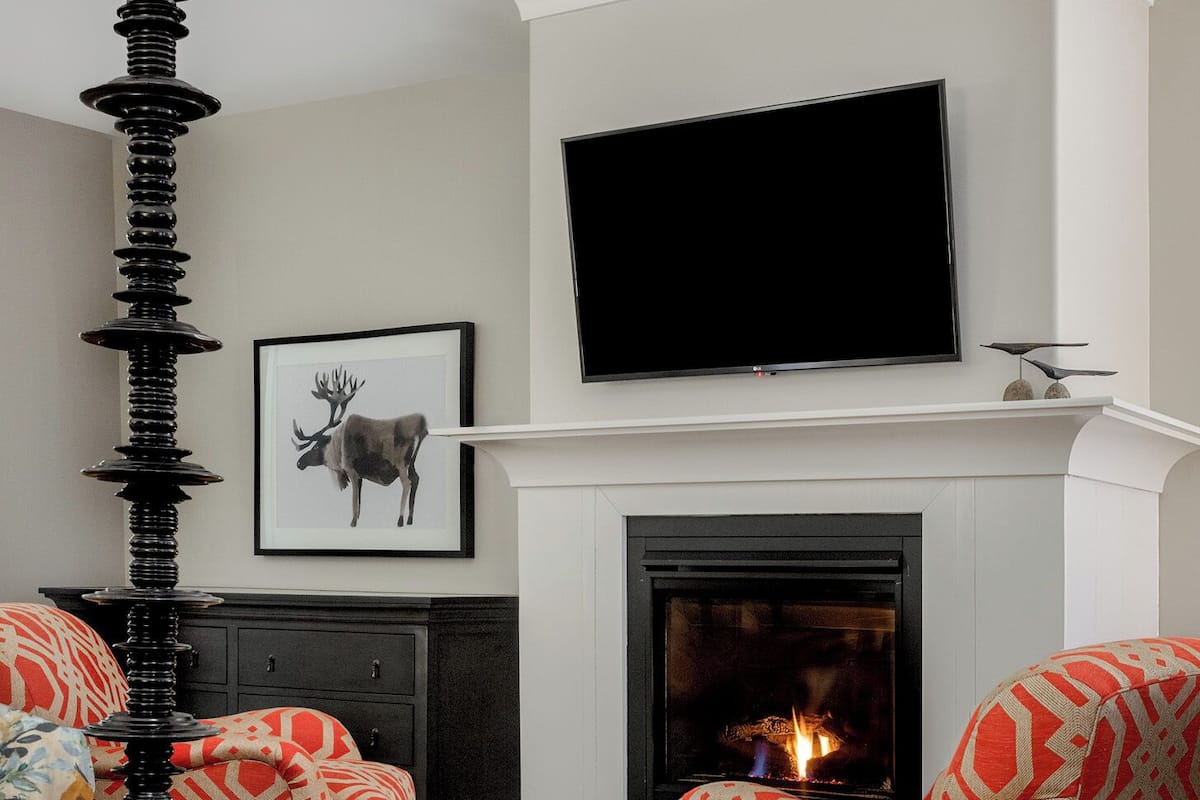 A living room with a fireplace, a television mounted above it, and two patterned armchairs.