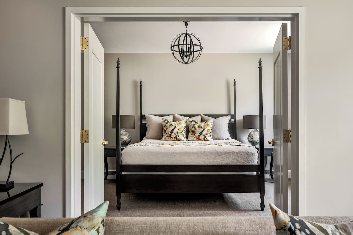 A bedroom with a four-poster bed, a chandelier, and a nightstand with a lamp.
