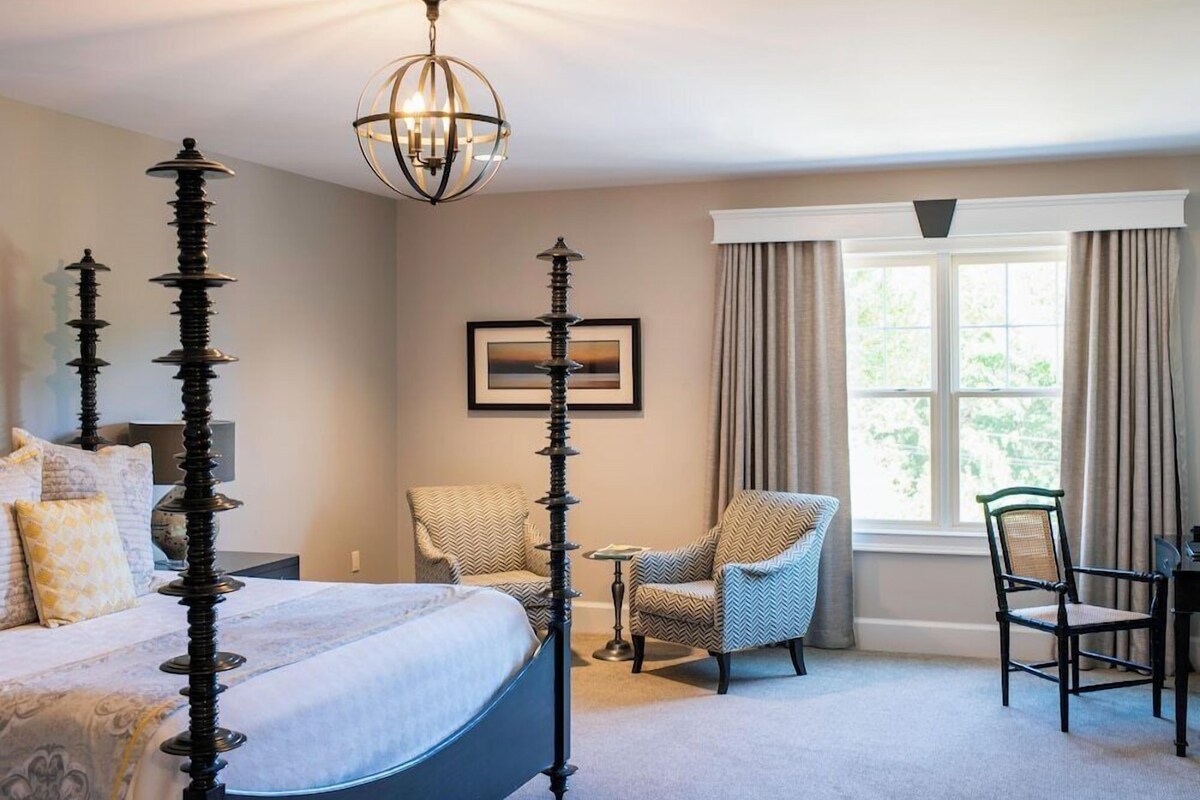 Une chambre à coucher avec un lit à baldaquin, un lustre, une chaise, une table et une fenêtre avec des rideaux.