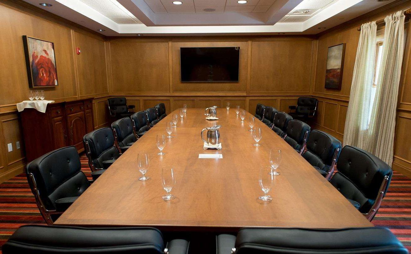 A conference room with a long table, black leather chairs, and a flat-screen TV on the wall.