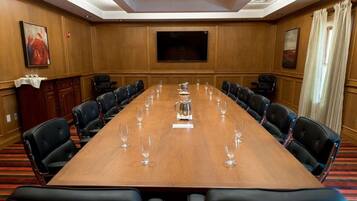 A conference room with a long table, black leather chairs, and a flat-screen TV on the wall.