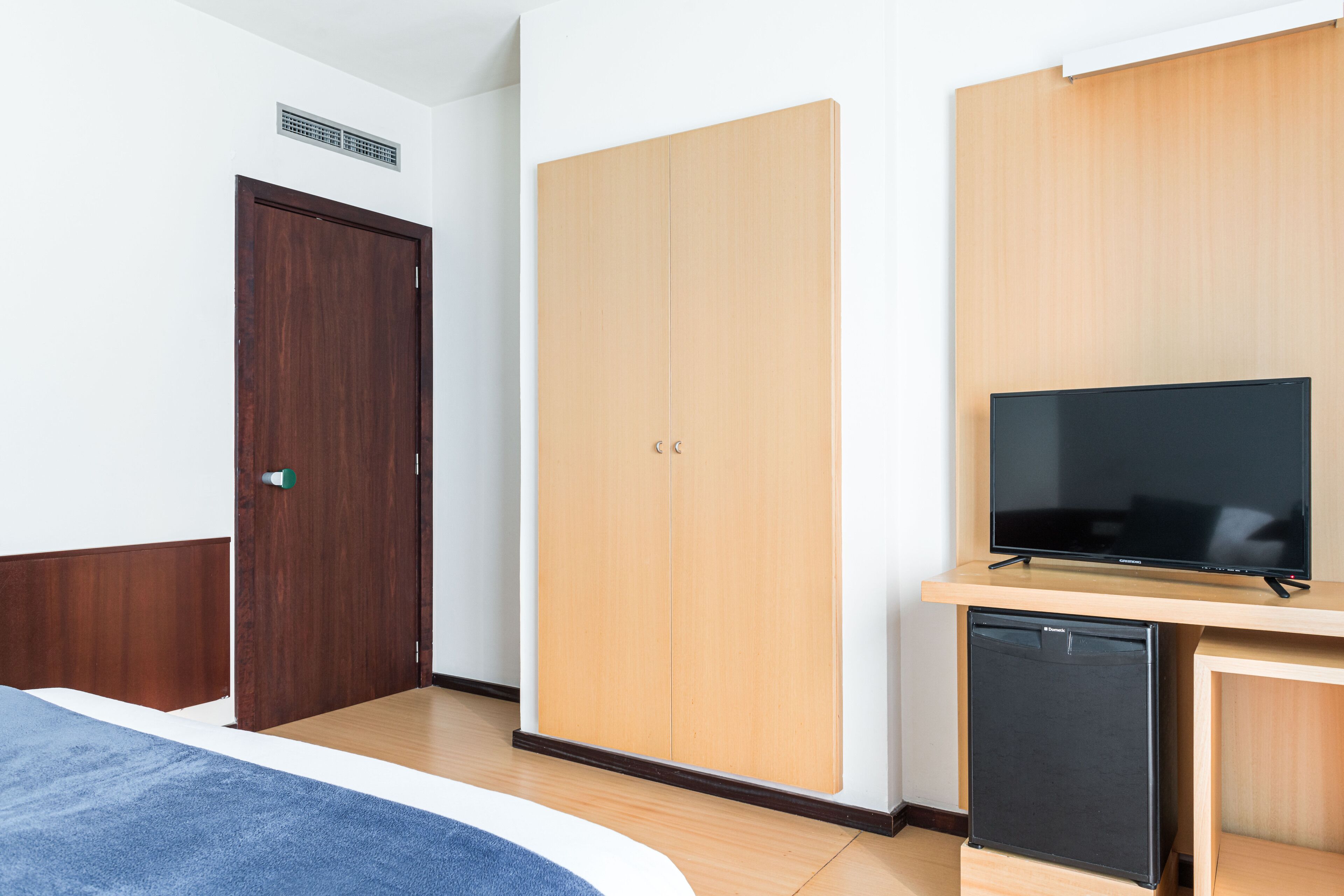 A hotel room with a bed, a wardrobe, a television, and a mini-fridge.