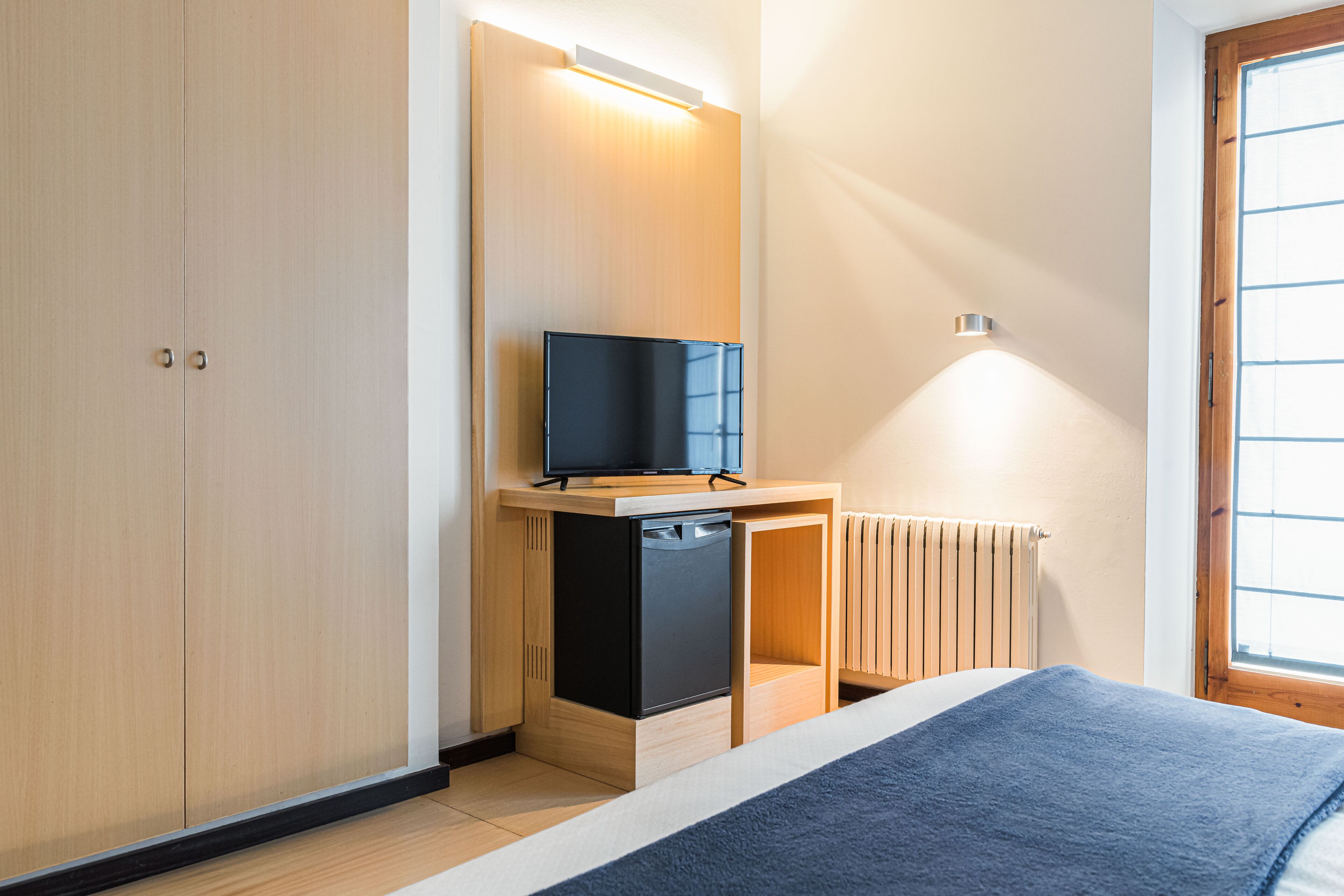 Een slaapkamer met een bed, een klein houten bureau en een televisie, en een raam.