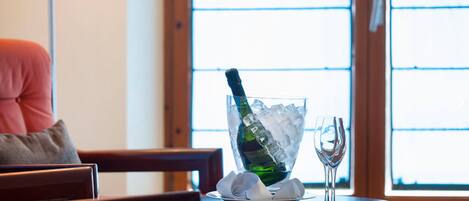 Una mesa con un bol de cristal que contiene una botella de champán y hielo, una copa de vino y un plato con una servilleta.
