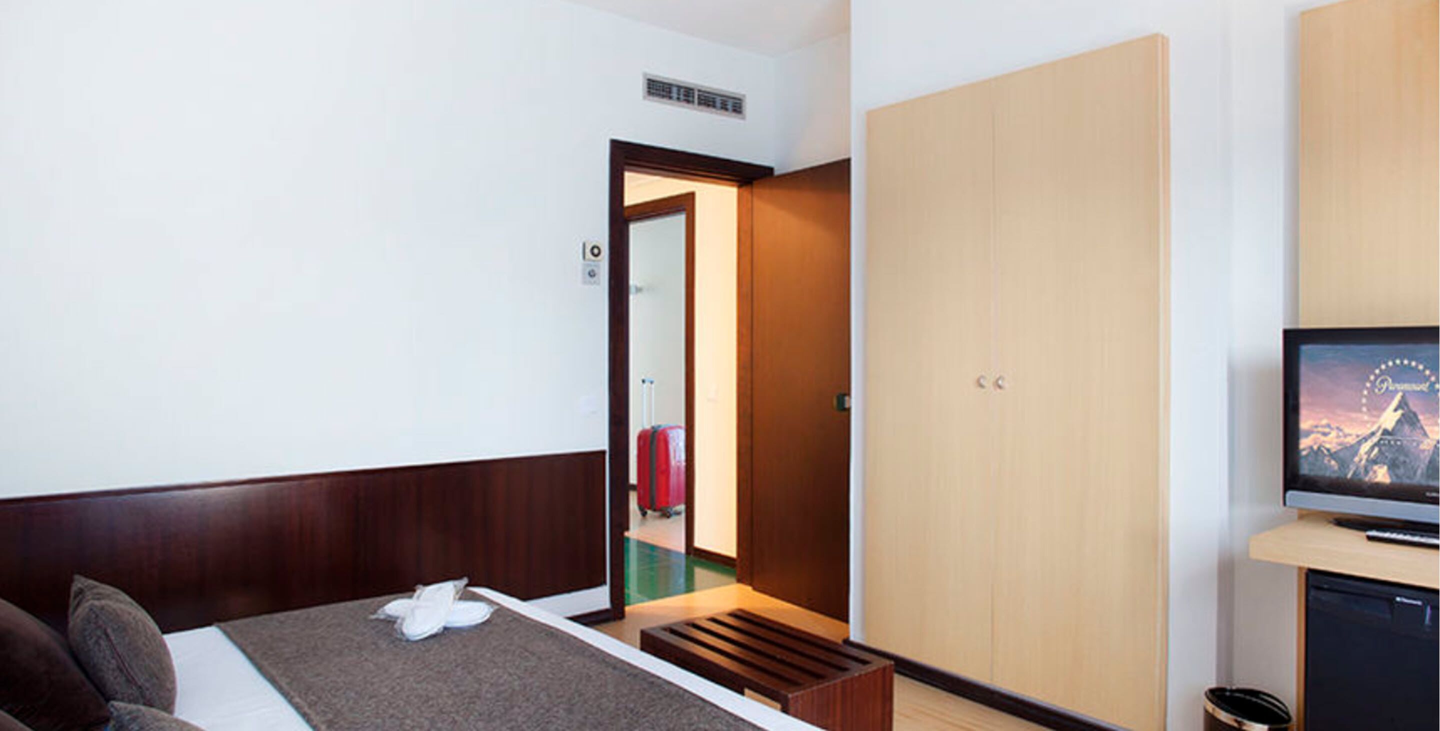 Habitació d'hotel amb un llit, una televisió, un armari i una maleta al fons.