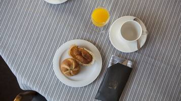 En frukostuppdukning med en randig duk, en tallrik med två bakverk, ett glas apelsinjuice, en kopp med tillhörande fat och en servett med en logotyp.