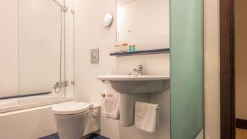 Et moderne badeværelse med et brusebadeværelse bag glas, et hvidt toilet, en vask med et spejl over og et blå flisegulv.