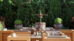 A wooden outdoor seating area with cushioned benches and a central wooden structure with a bottle and glasses. - Hotel Empordà (Figueres)
