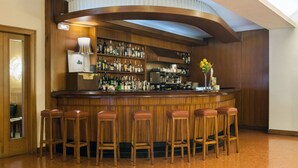 A bar area with wooden bar stools, a counter with various bottles, and a wall-mounted lamp. - Hotel Empordà (Figueres)