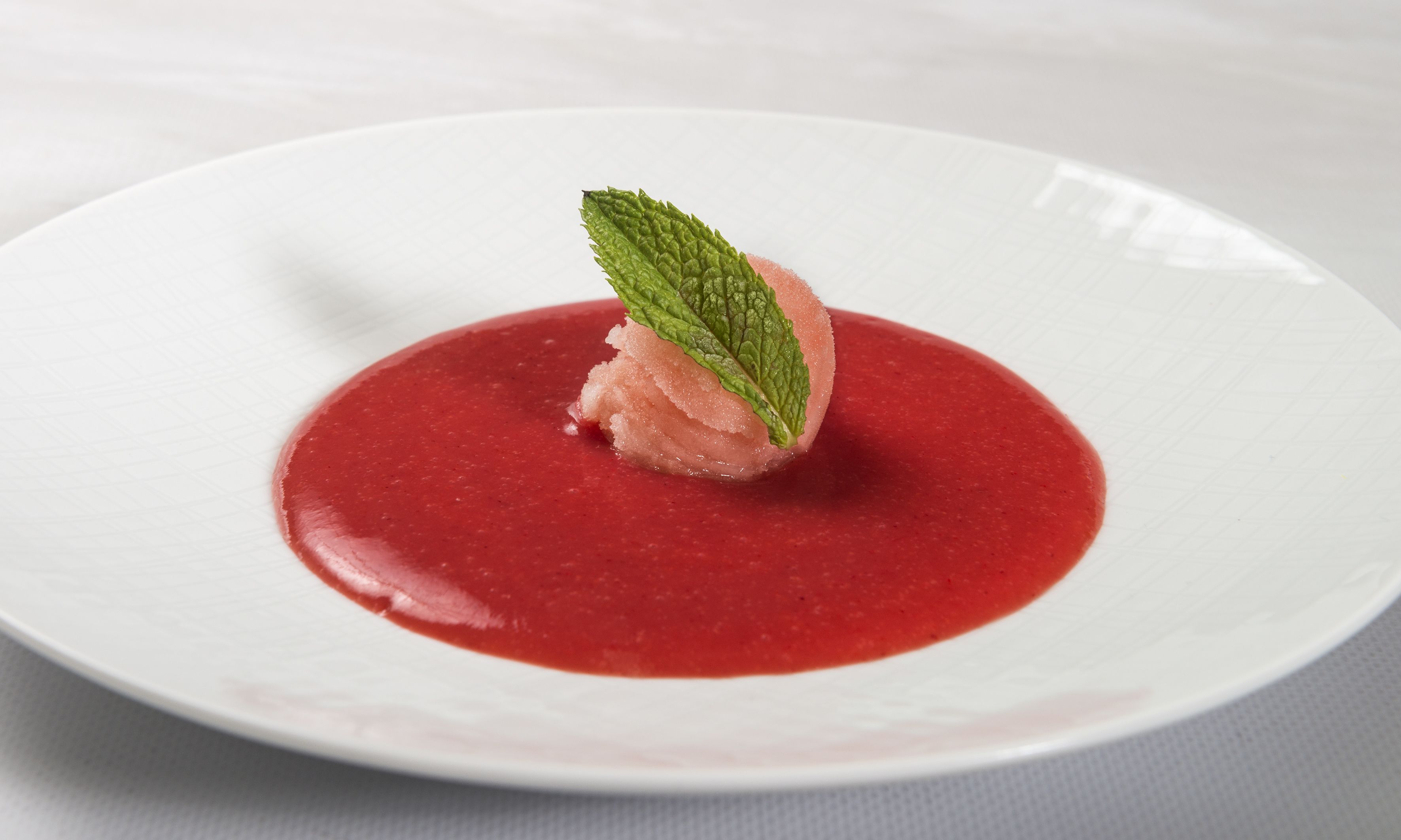 A dessert on a white plate with a red sauce and a mint leaf garnish.