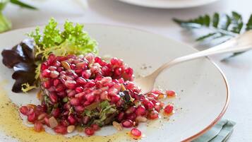 A plate with a salad of pomegranate seeds, greens, and nuts, accompanied by a spoon.