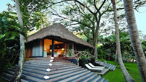 Un bungalow au toit de chaume, doté d’une terrasse en bois, entouré d’une végétation luxuriante.