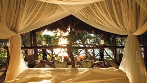 Un lit recouvert de draps blancs, dans une structure au toit de chaume, avec vue sur la mer.