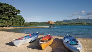 Three kayaks on a sandy beach with a thatched-roof hut in the background.