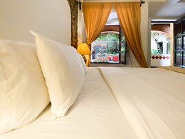 Habitación de hotel con cama, cortinas y vista a un espacio exterior con plantas y una silla roja.