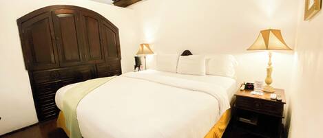 Un dormitorio con una cama grande, cabecera de madera, dos mesitas de noche con lámparas y techo de madera.