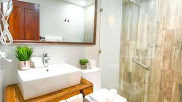 A modern bathroom with a large mirror, a wooden vanity, a white sink, a toilet, and a glass shower enclosure.
