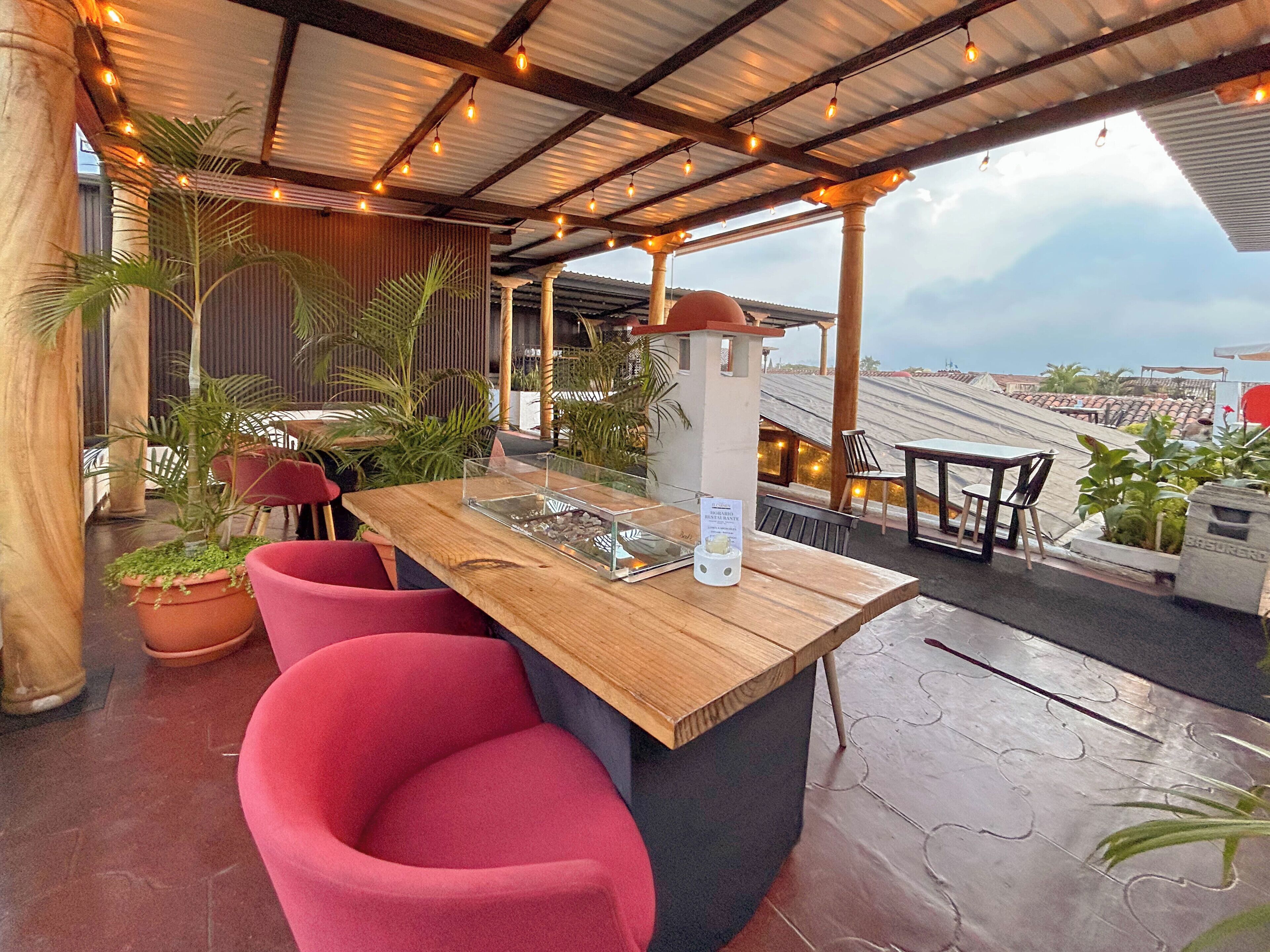 Un bar situé sur un toit, avec une table en bois, des chaises rouges et des plantes en pot.