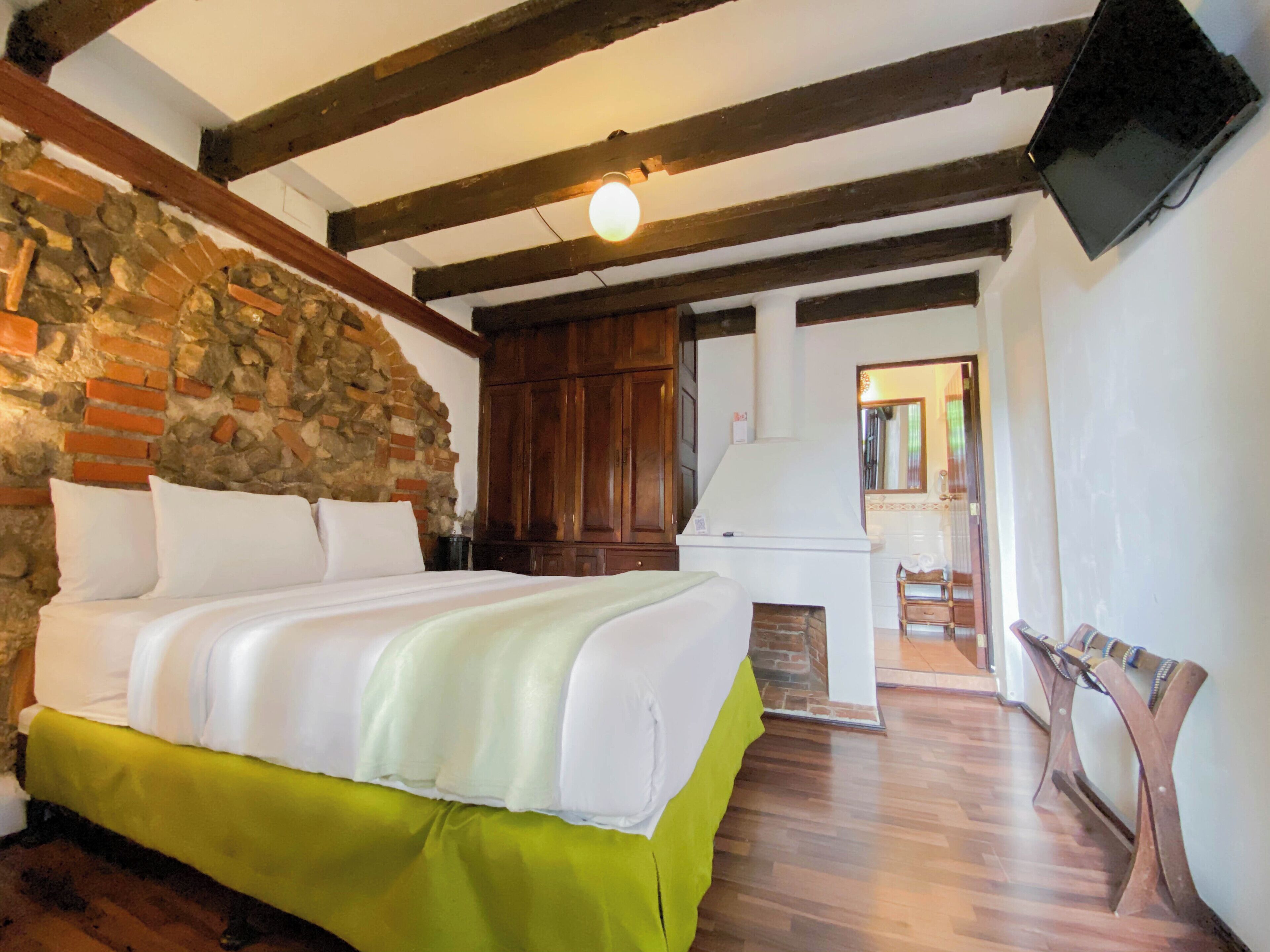 Ein Zimmer mit einem Bett, einer Steinwand, Holzbalken, einem Kamin und einem Fernseher.
