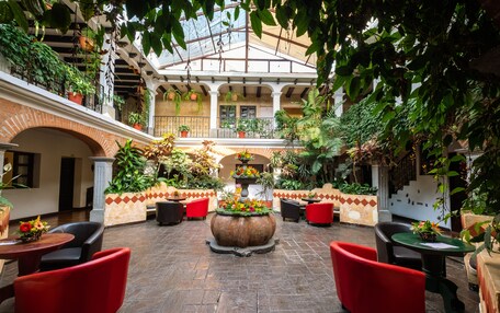 A spacious courtyard with red chairs and tables, surrounded by lush greenery and potted plants.
