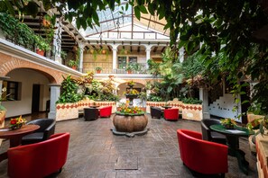Un amplio patio con sillas y mesas rojas, rodeado de abundante vegetación y plantas en macetas.