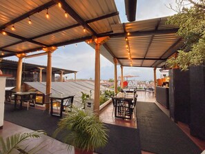 Eine Terrassenanlage mit Tischen und Stühlen, eine überdachte Sitzgelegenheit und Kübelpflanzen.