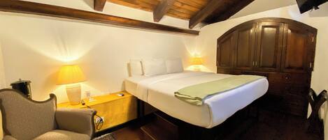 A hotel room with a wooden ceiling, a bed with white linens, a nightstand with a lamp, a chair, and a wardrobe.