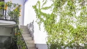 Un bâtiment blanc avec un escalier menant à un balcon, entouré de plantes en pot et de verdure.