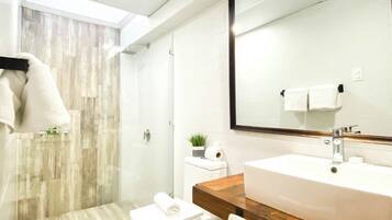 Une salle de bain moderne avec un grand miroir, un meuble-lavabo en bois, un lavabo blanc et un espace douche.
