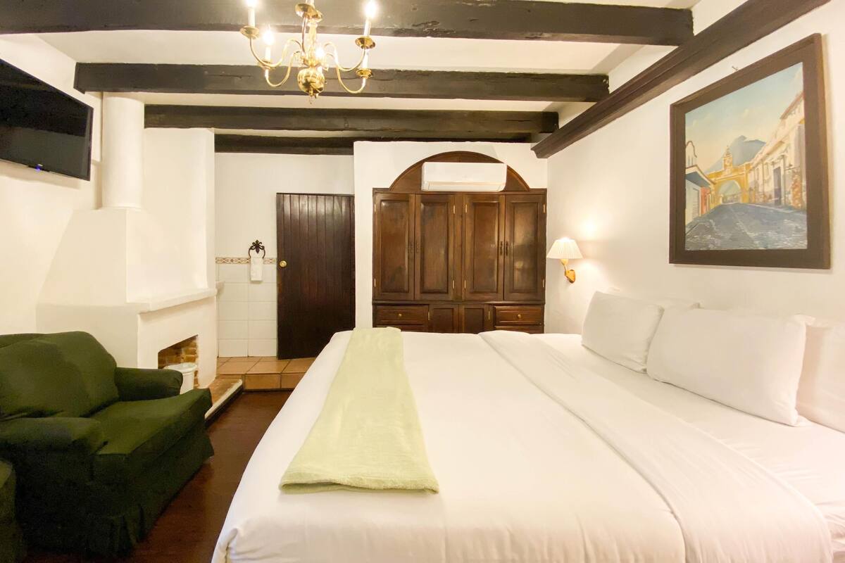Een hotelkamer met een groot bed, een groene fauteuil, een houten garderobe, een kroonluchter en een schilderij aan de muur.