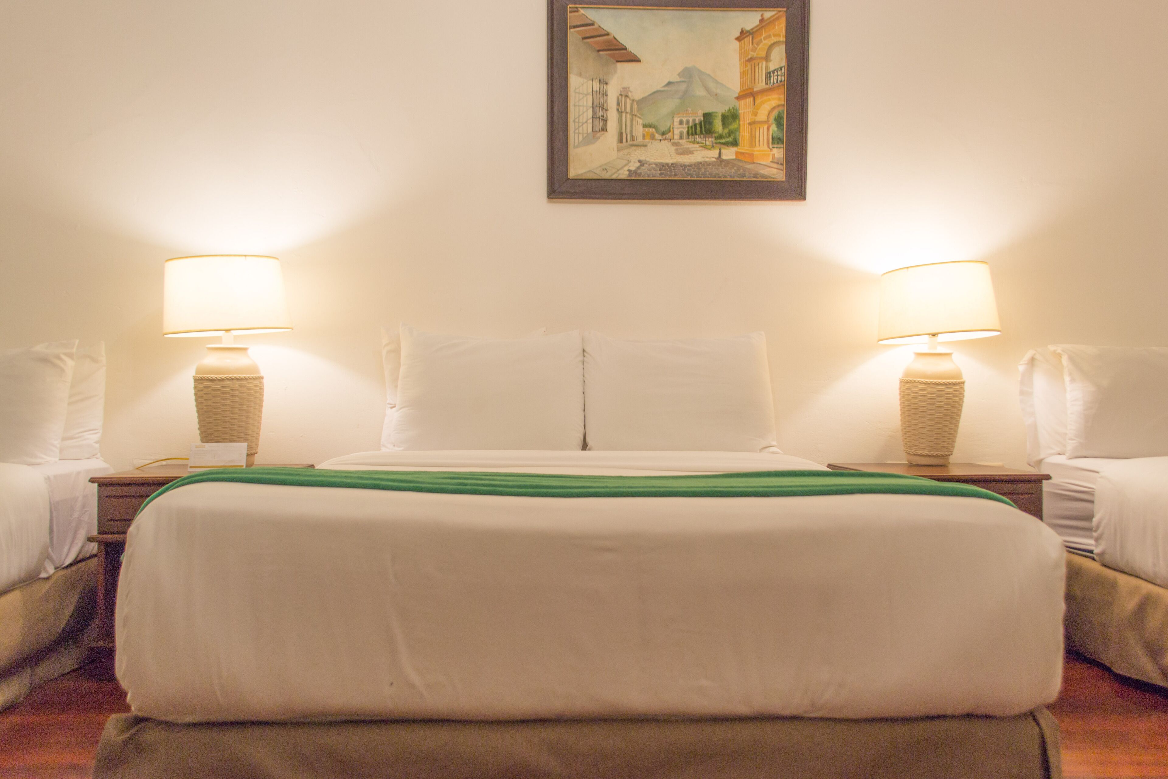 A hotel room with a bed, two bedside tables, two lamps, and a painting on the wall.