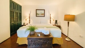 Une chambre à coucher bien rangée, avec un lit, des lampes de chevet, une table de chevet ornée d’une plante, un tableau accroché au mur et un lampadaire.