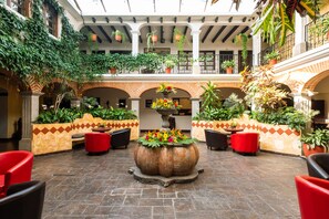 Un patio con una fuente central, asientos rojos y plantas en macetas.