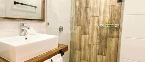 A modern bathroom with a large mirror, white sink, wooden vanity, and a shower area with wooden tiles.