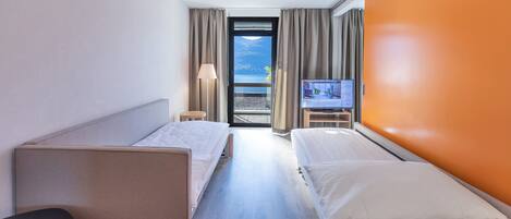 A hotel room with two beds, a TV, a desk, and a view of the sea.