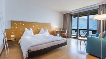 A modern hotel room with a bed, desk, and balcony with a view.